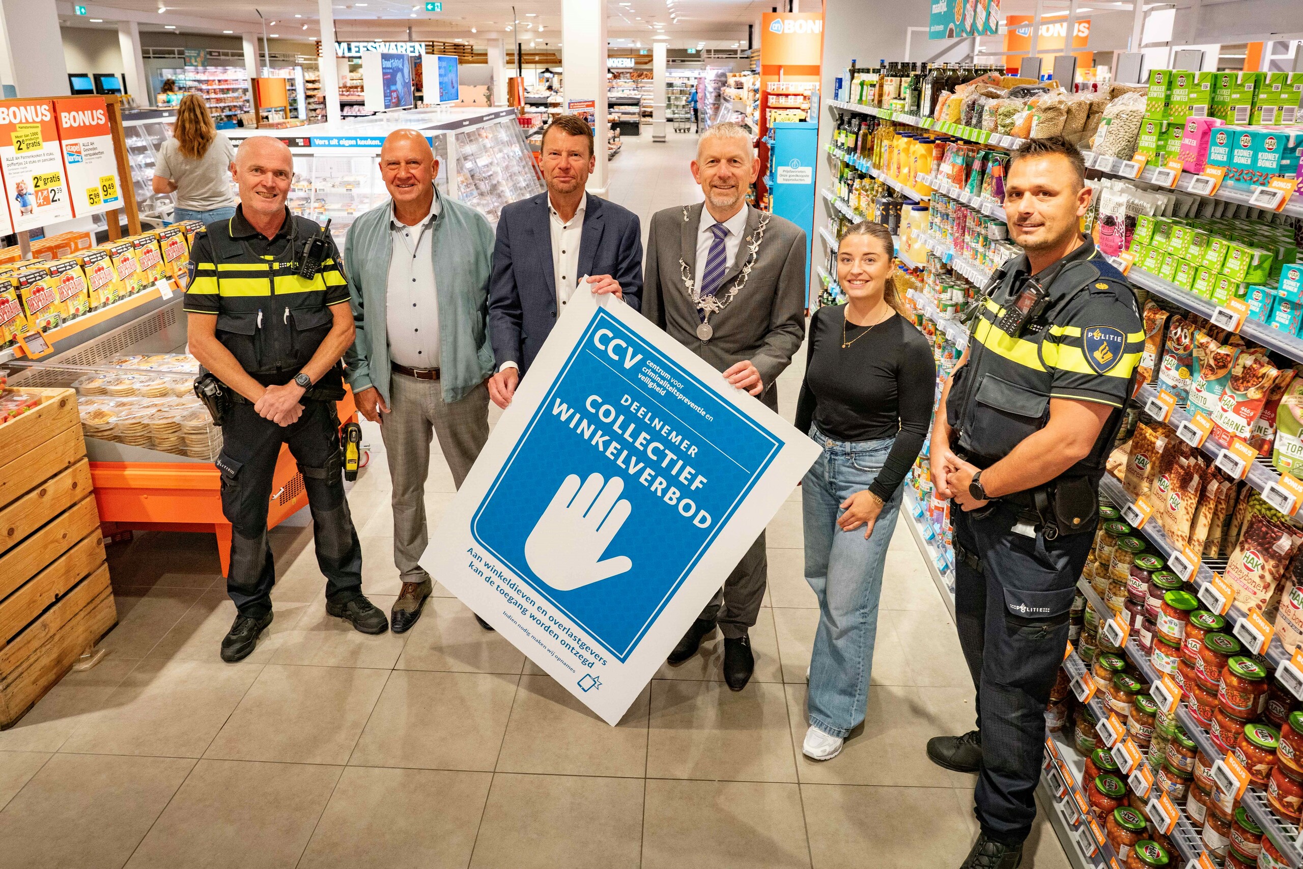Wijkagent Mark Krom, Fons Sijnesael van Platform Veilig Ondernemen, ondernemer Jacco Kat  van de Albert Heijn, burgemeester Jan de Boer, Joy Vonk van gemeente Den Helder, operationeel expert  wijkagent Patrick van der Hout laten de sticker zien waaraan het ‘collectief winkelverbod’ te herkennen is. Foto: RedMous