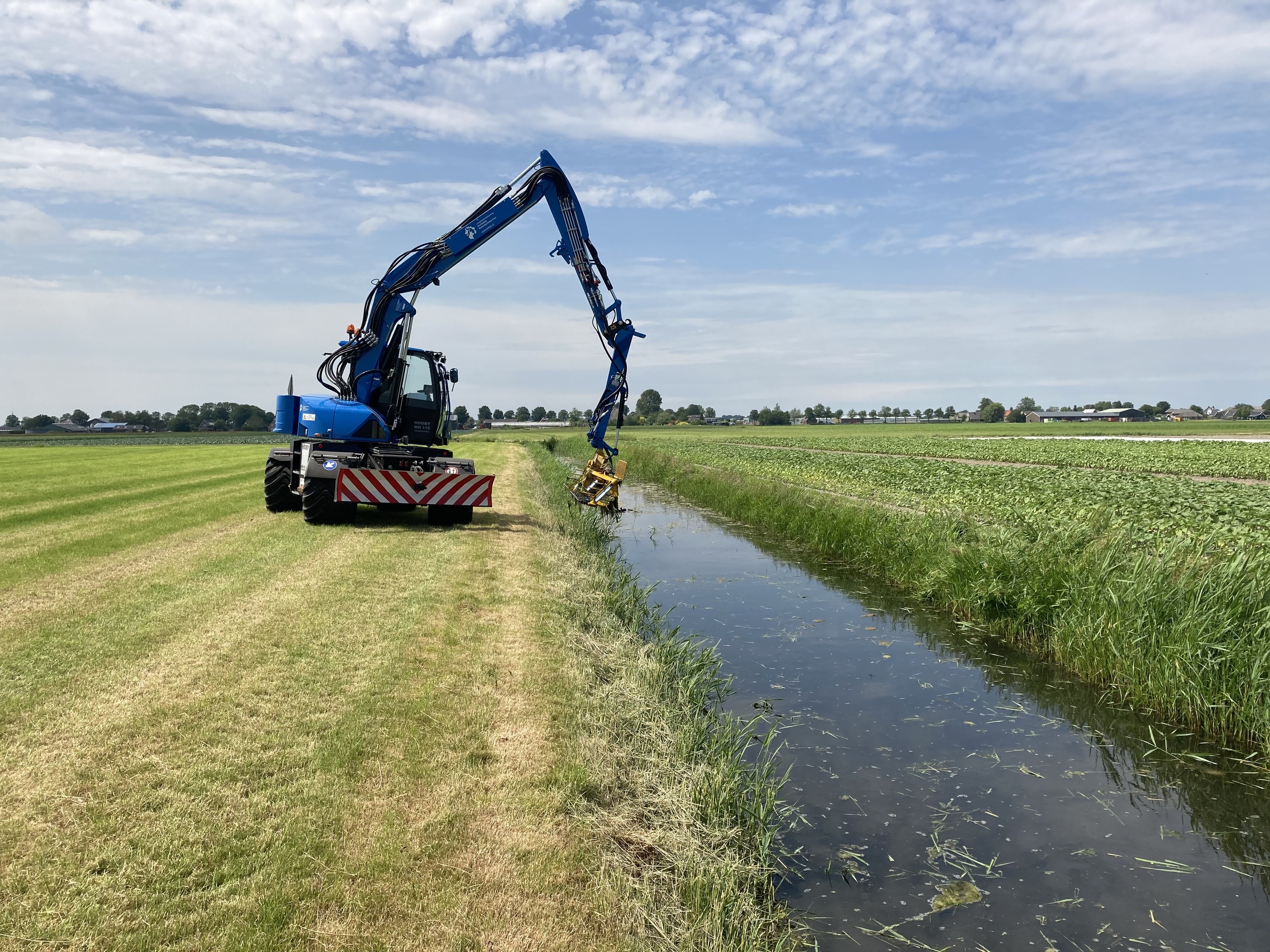 Een medewerker van HHNK verwijdert riet en waterplanten uit een sloot